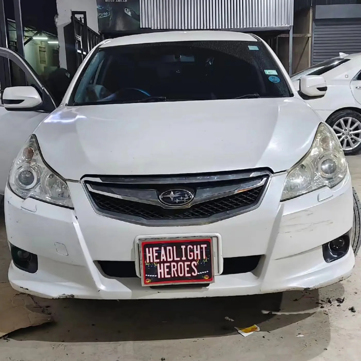 White Subaru Legacy at the workshop with headlights off